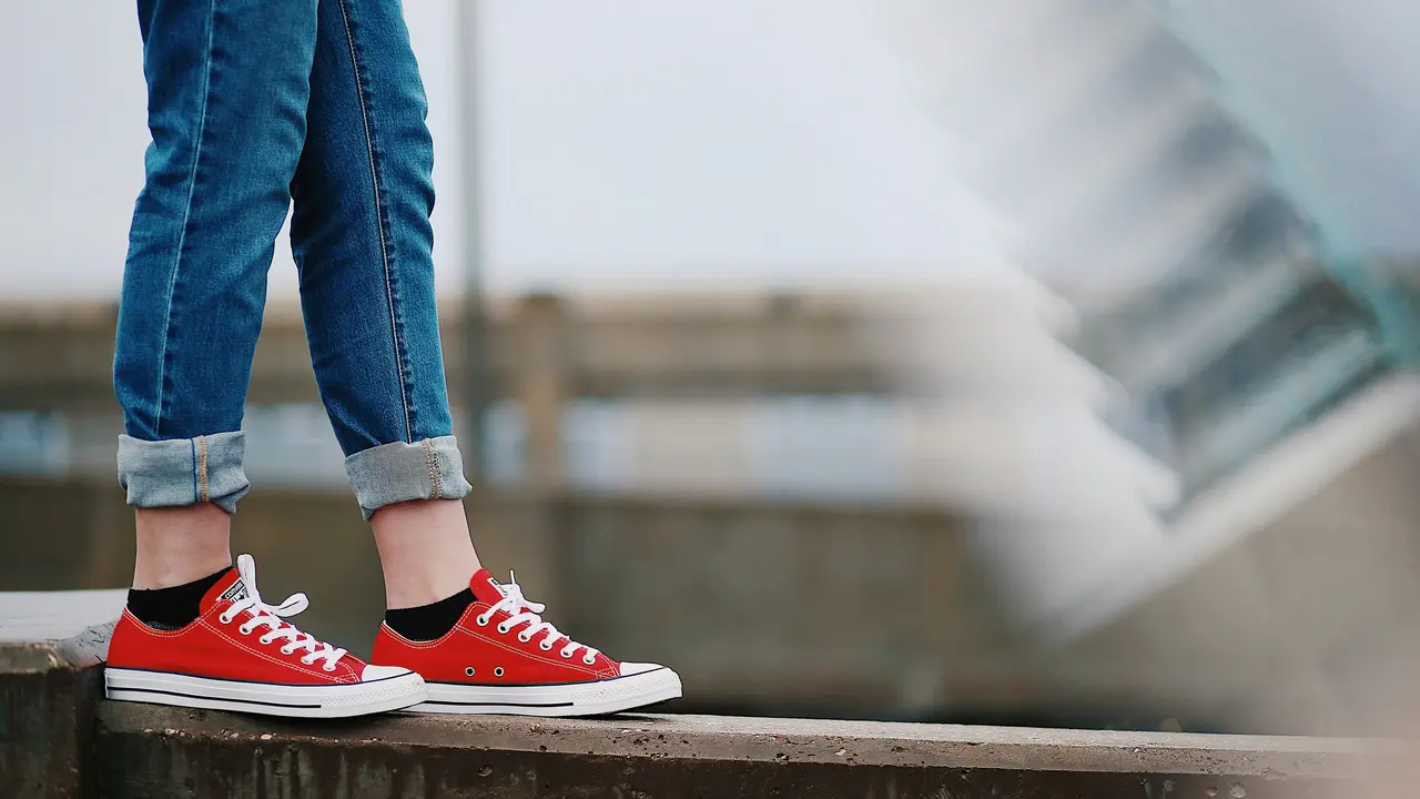 Mensch mit roten Turnschuhen balanciert auf einer Mauer
