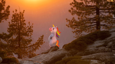 Eine Person in einem Einhornkostüm steht auf einem Felsen und Blickt der untergehenden Sonne entgegen.