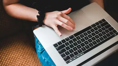 Eine junge Person hat einen Laptop auf dem Schoß und tippt